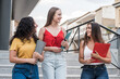 Young female latina college students, talking and walking happily, outside the university campus building. These three smiling women discuss what they are learning in college