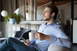 © fizkes - Side view peaceful young happy businessman relaxing on comfortable armchair with cup of hot tea coffee, enjoying pause break time or thinking of company strategic development alone in office.