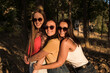 Three beautiful young women in sunglasses are smiling hugging in the field on a sunny afternoon. Happy girls in the field in summer