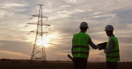 Wall Mural - engineers on a tablet discuss a high-voltage power line, look and point at an electric pole, shake h