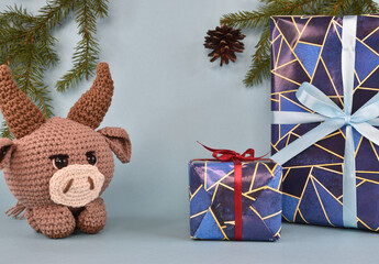 Wall Mural - A brown knitted New Year's bull stands next to wrapped New Year's gifts. Behind him hangs a cone from a spruce branch.