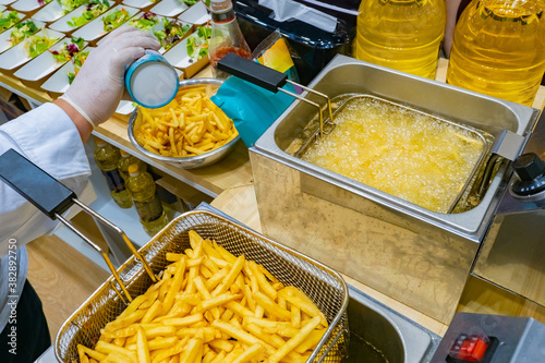 Preparation of potato dishes. Fast food restaurant. Industrial deep fryer. The cook is ready to prepare portions of food. Potatoes are fried in dripping oil. French fries on the menu.