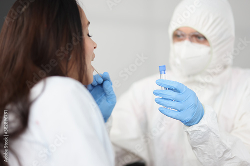 Doctor in white antiplague suit takes swab from his throat with cotton swab into test tube in apartment. Diagnostics testing of patients covid 19 concept.