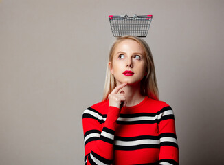 Canvas Print - Style blonde in red sweater with basket on her head on grey background