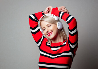 Wall Mural - Style girl in red sweater with headphones on grey background