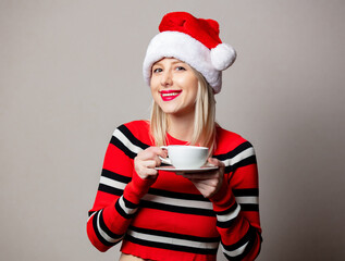 Wall Mural - Smiling girl in Christmas hat with cup of coffee on grey background