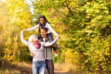 Wall Mural - Happy family having fun outdoors in autumn park against blurred leaves background