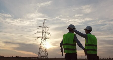 Wall Mural - an engineer enters the frame, points at a high-voltage pole against the backdrop of sunset and hugs 