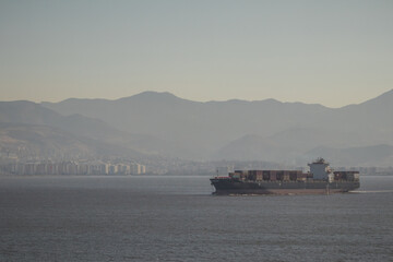 A big container cargo ship or carrier traveling from the Port of Izmir in Turkey towards Athens on a cloudy day. Heavy loaded container ship with colorful containers.