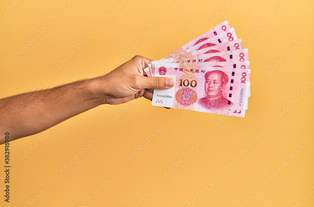 Hand of hispanic man holding chinese 100 yuan banknotes over isolated yellow background.
