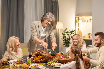 Wall Mural - Bearded mature man cutting homemade roasted turkey in the center of table