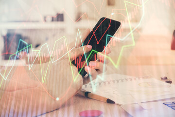 Double exposure of man's hands holding and using a digital device and forex graph drawing. Financial market concept.