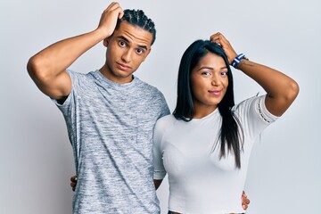 Wall Mural - Young latin couple wearing casual clothes confuse and wondering about question. uncertain with doubt, thinking with hand on head. pensive concept.