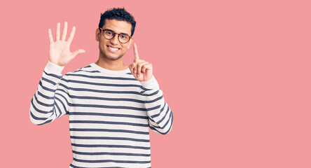 Wall Mural - Hispanic handsome young man wearing casual clothes and glasses showing and pointing up with fingers number six while smiling confident and happy.