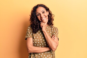 Wall Mural - Middle age beautiful woman wearing casual t shirt smiling looking confident at the camera with crossed arms and hand on chin. thinking positive.