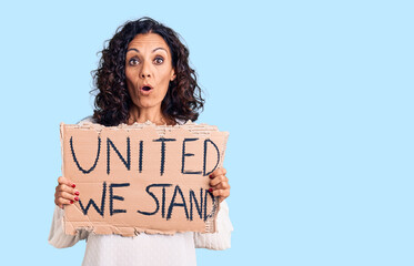 Poster - Middle age beautiful woman holding united we stand banner scared and amazed with open mouth for surprise, disbelief face