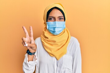 young brunette arab woman wearing traditional islamic hijab and medical mask smiling with happy face