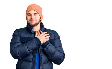 Young handsome man wearing winter clothes smiling with hands on chest with closed eyes and grateful gesture on face. health concept.