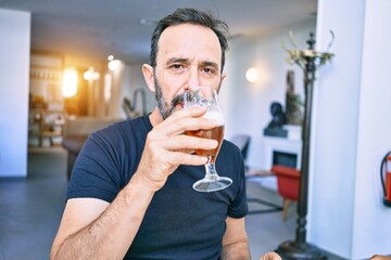 Middle age handsome man wearing casual tshirt. Drinking glass of beer at restaurant