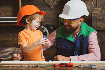 Wall Mural - Little son helping his father with building work. Parent in protective helmet teaching little son to use different tools in school workshop.