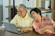 © Supagrit Ninkaesorn - Senior Asian elderly couple in home casual outfit with happy smiling emotion sitting in living room using laptop and tablet together