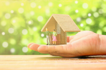 figure man and woman standing in front of coins stack with small wood roof , home loan concept