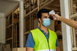 © twinsterphoto - Young Indian factory warehouse worker wearing face mask getting body temperature check with infrared thermometer scanner before working. Security measure at workplace in Coronavirus Covid 19 pandemic