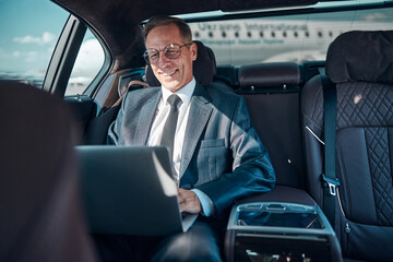 Smiling businessman using laptop in car after landing