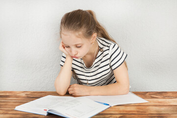 Wall Mural - Girl 8 - 10 years old doing homework sitting at a wooden table. Homeschooling