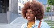 © VAKSMANV - Portrait of African American young pretty hipster woman standing at city street and smiling joyfully to camera. Close up of beautiful happy cheerful curly female outside.