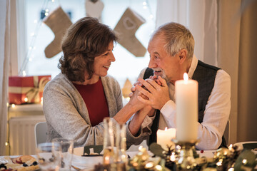 Wall Mural - Happy senior couple indoors at home sitting at the table at Christmas, talking.