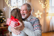 © Halfpoint - Young woman giving present to happy grandfather indoors at home at Christmas.