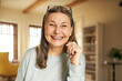 © shurkin_son - Close up image of happy beautiful energetic senior woman with wrinkles and gray long hair enjoying nice time indoors posing in cozy living room interior, looking and smiling broadly at camera