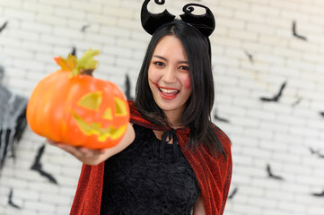 Portrait of beautiful young asian woman wearing witch costume holding pumpkin Jack O Lantern on background decorated for Halloween