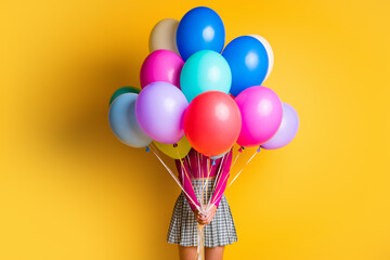 Poster - Portrait photo of funny girl making surprise hiding face keeping colorful balloons wearing casual clothes isolated on yellow color background