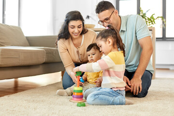 family and people concept - happy mother, father, little daughter and baby son playing with pyramid toy at home