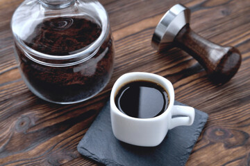 Wall Mural - coffee in a cup on a stone stand, glass jar with coffee beans and coffee tamper, wooden natural background