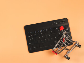  flat lay of computer keyboard with shopping cart on orange background  with copy space. Shopping online concept.