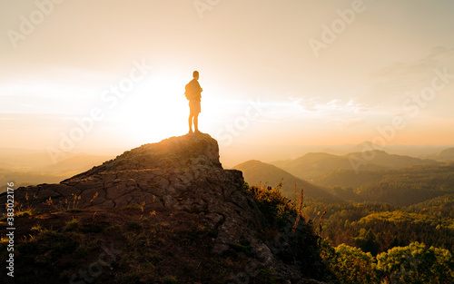 Fotografía Silhouette man hiker on top of a rocky mountain cliff overlooking the beautiful Czech Nature Landscape during a colorful sunny sunset