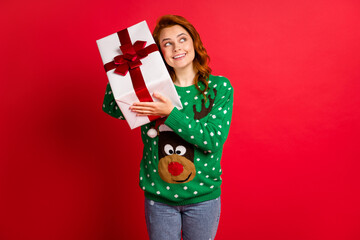 Photo portrait of woman holding present to ear listening inside shaking guessing isolated on vivid red colored background