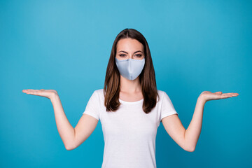 Poster - Photo of pretty lady good mood hold open palms arms showing select pick novelty covid infection stop products wear medical mask casual white t-shirt isolated blue color background