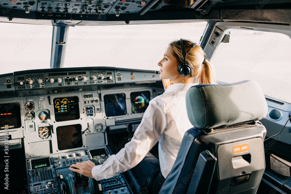 Woman pilot sitting in airplane cockpit, wearing headset. - obrazy, fototapety, plakaty 