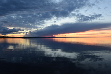Wall Mural - Sunlight in the dark clouds of the twilight sky is reflected in the calming water of the lake