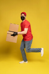 Wall Mural - Delivery man in protective mask and gloves with box in studio isolated on yellow background