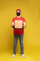 Wall Mural - Delivery man in protective mask and gloves with box in studio isolated on yellow background