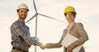 © VAKSMANV - Caucasian man engineer and woman environmental consultant in helmets shaking hands and smiling to the camera on the windmill turbine background. Portrait.