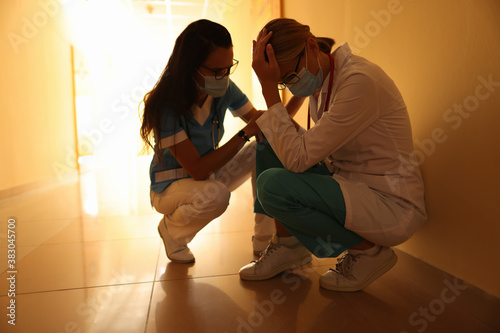 Nurse calms crying doctor in uniform and medical masks and sits in hospital corridor. Medical error concept.