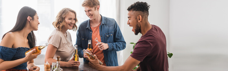 panoramic concept of multiethnic friends with bottles of beer talking during party