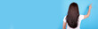 © Sviatoslav Kovtun - Brunette girl with long hair pointing with finger, view from behind. Isolated on blue background, copy space template, banner.