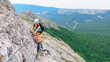 © Tropical studio - Young mother, child in safety equipment climb to mount top by via ferrata beginner route. Family travel adventure, hiking activity. Kids exploring nature on summer vacation. Weekend day walking tour